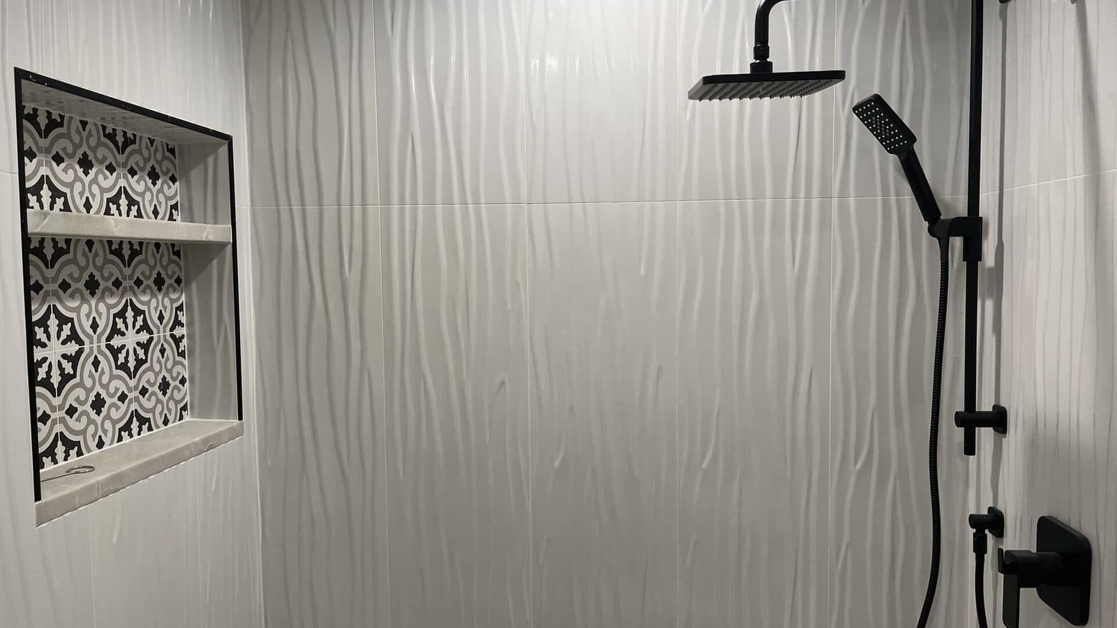 Tile detail cost difference: a Red Bank NJ shower niche finished with a black metal edge profile and stone shelf beside cut-in valve trim on ribbed white wall tile